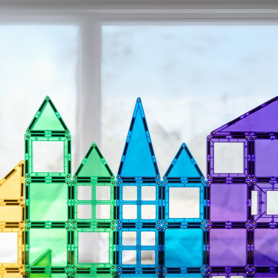 Een skyline van regenboogkleurige gebouwen gemaakt van Connetix magnetische tegels voor een raam.