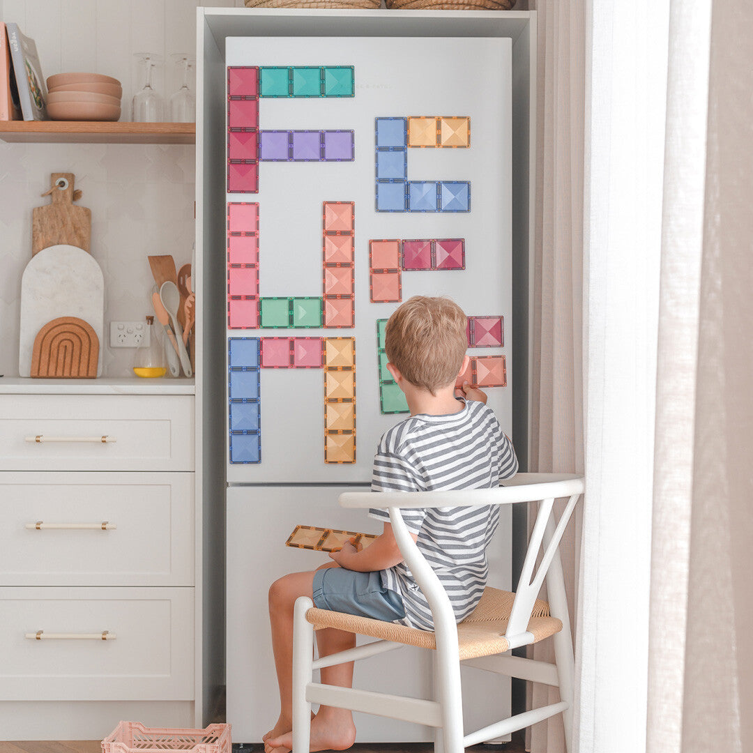 Een jongen speelt met Connetix magnetische tegels op een witte koelkast.