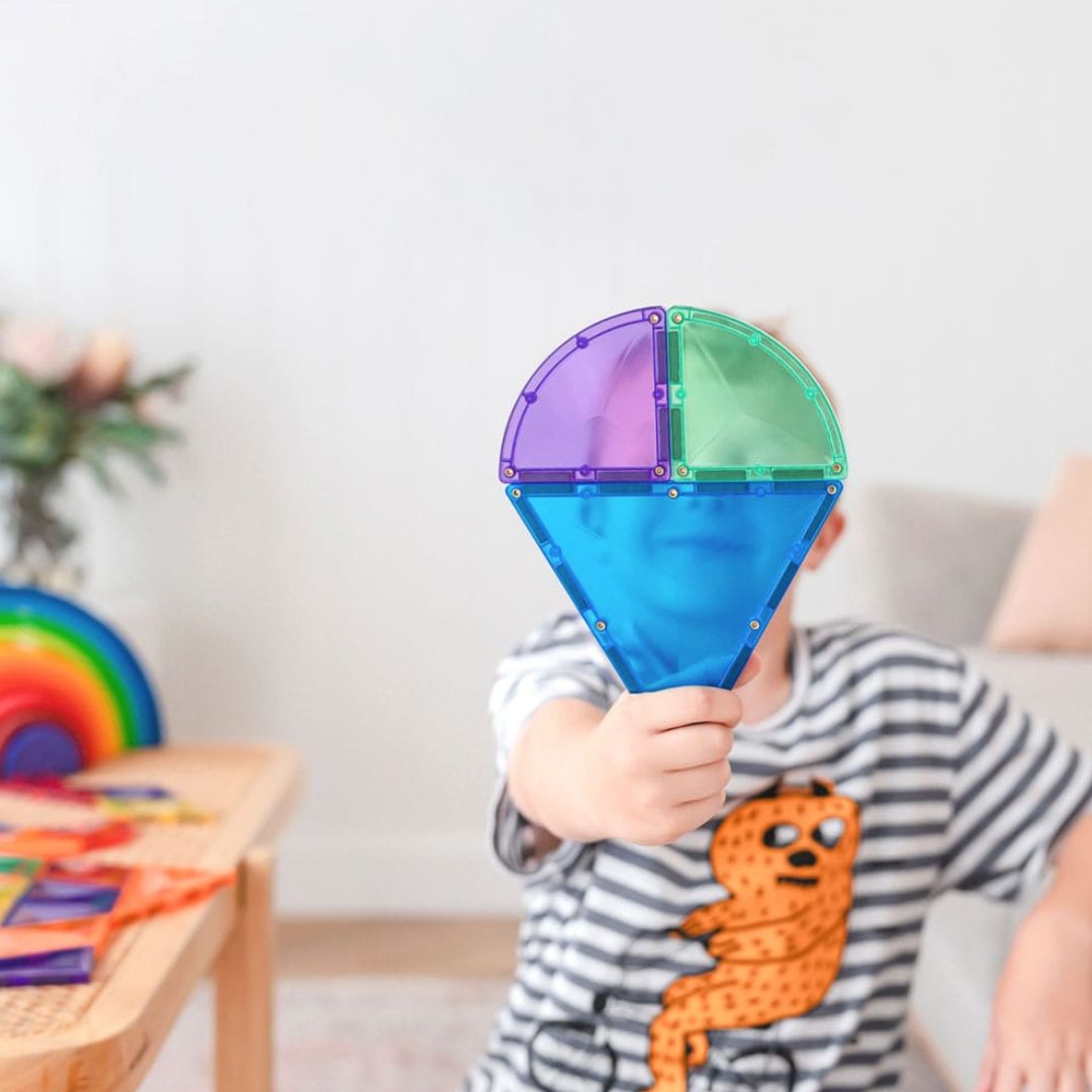 Een kind houdt een kleine constructie van Connetix magnetische tegels in regenboogkleuren omhoog.