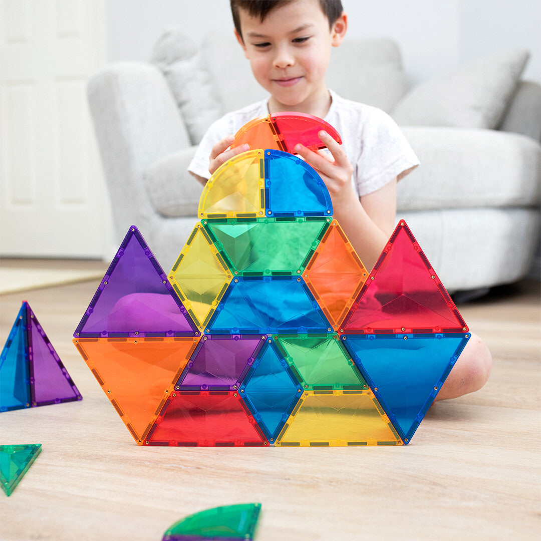 Een kind voegt een tegel toe aan een grote constructie van Connetix magnetische tegels in regenboogkleuren.