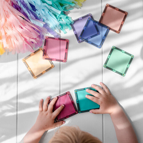 Kinderhanden spelen met Connetix magnetische tegels in pastelkleuren op een witte tafel.