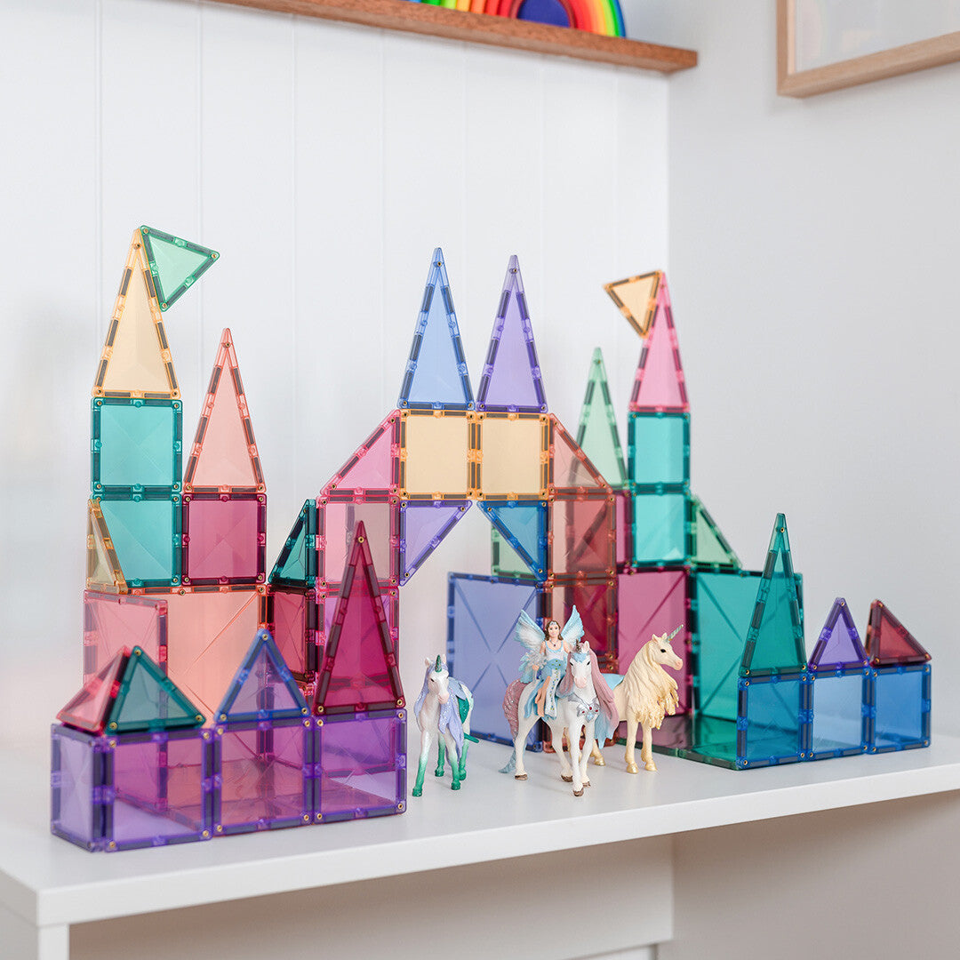 Een kasteel gebouwd van Connetix pastel magnetische tegels met eenhoornfiguren ernaast.
