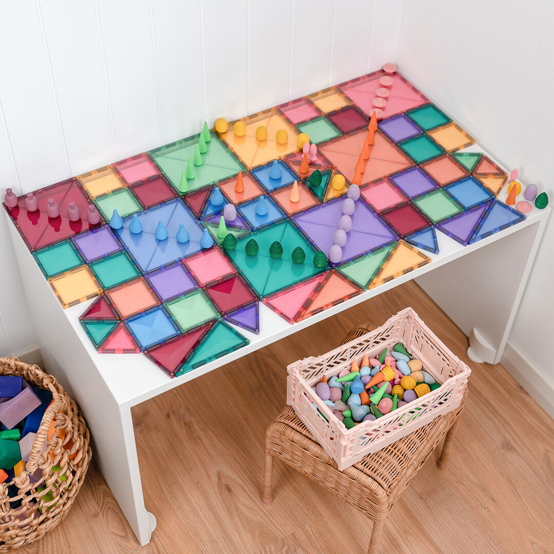 Een tafel bedekt met een plat patroon van Connetix pastel magnetische tegels en kleine houten speelstukken.