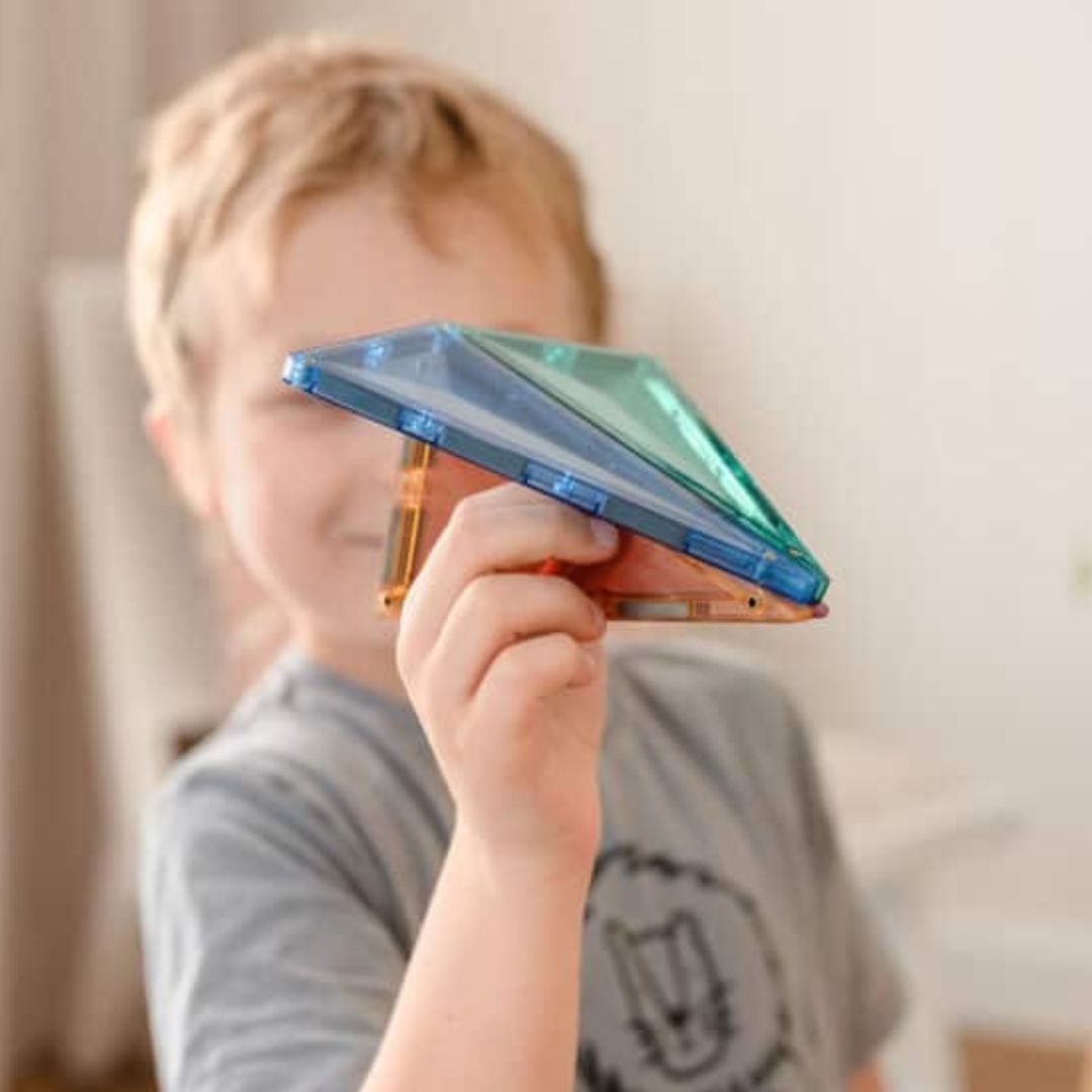 Een kind houdt twee Connetix magnetische tegels in pastelkleuren voor zijn gezicht.