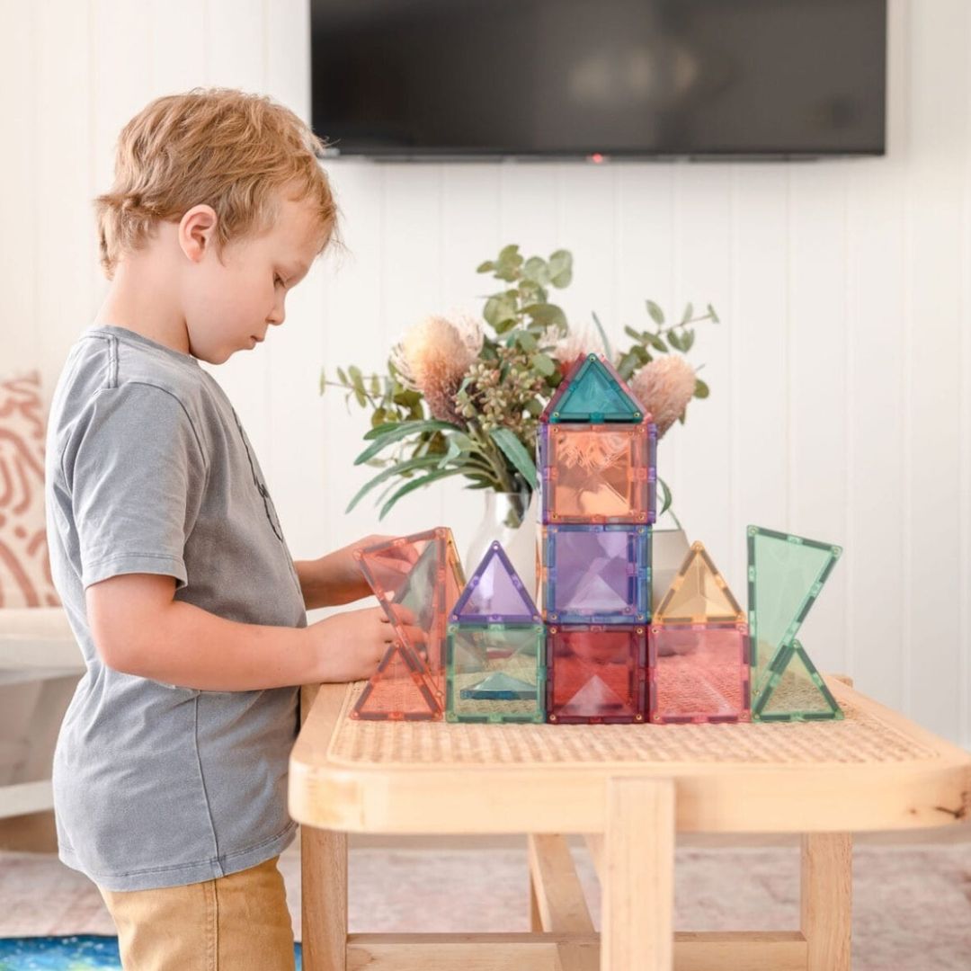 Een kind bouwt structuren met Connetix pastel magnetische tegels op een houten tafeltje.