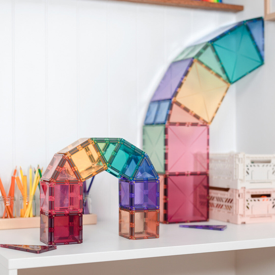 Een boog en een gebogen muur gebouwd van Connetix pastel magnetische tegels op een witte plank.