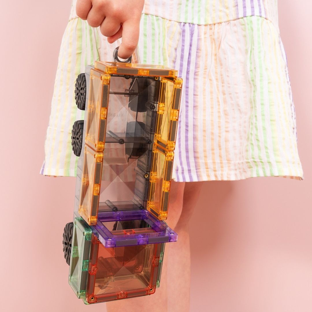 Een kind houdt een Connetix vrachtwagen vast, gemaakt van pastelkleurige magnetische tegels, van de zijkant gezien.