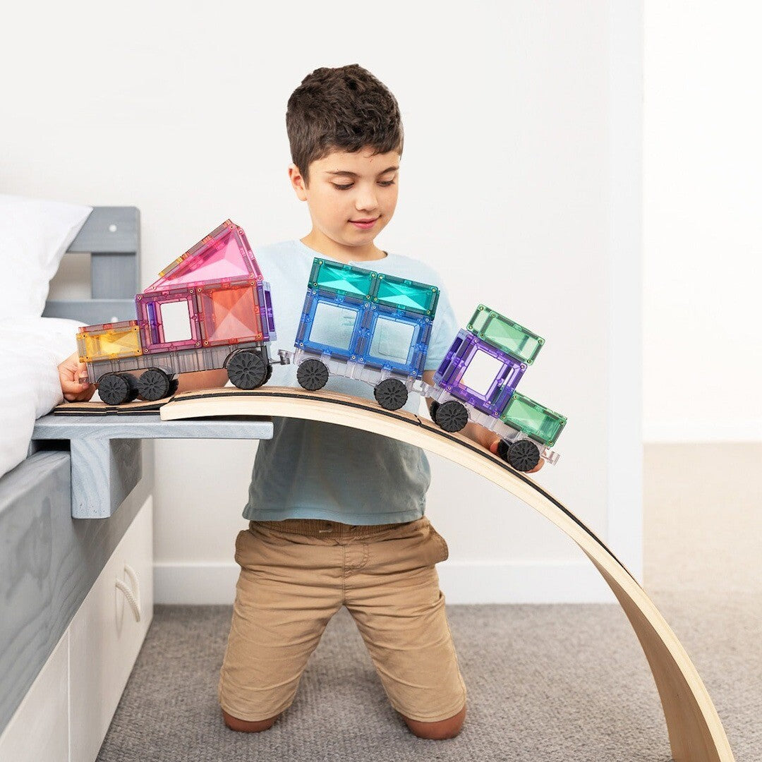 Een jongen speelt met een Connetix trein, gemaakt van pastelkleurige magnetische tegels, op een houten balansbord.