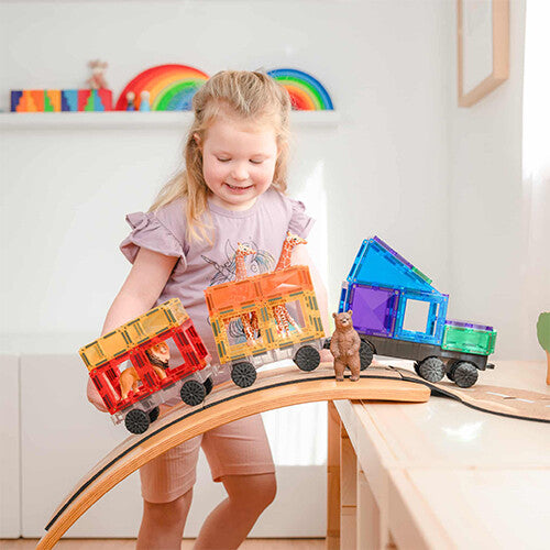 Een lachend kind speelt met Connetix magnetische tegels, een trein met dierenwagons op een houten balansbord.