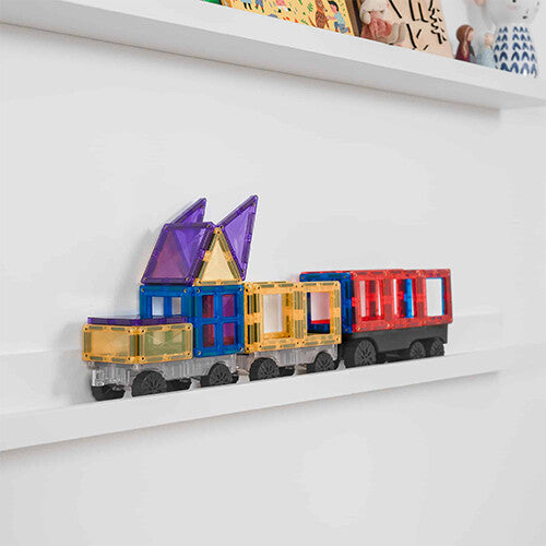Een lange trein gemaakt van Connetix magnetische tegels in regenboogkleuren staat op een witte plank.