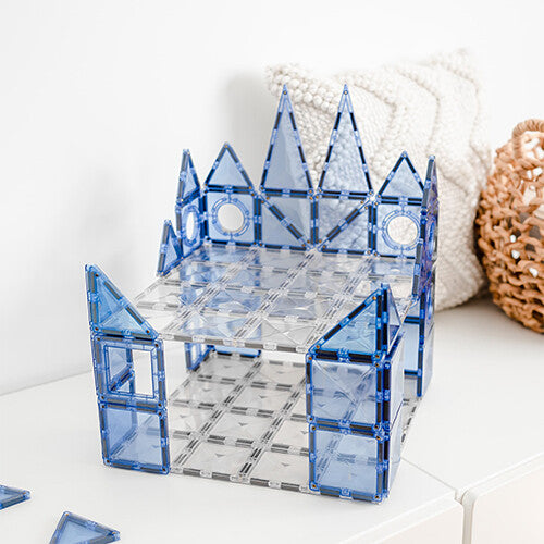 Een kasteelachtig gebouw gemaakt van transparante en blauwe Connetix magnetische bouwplaten staat op een witte kast.