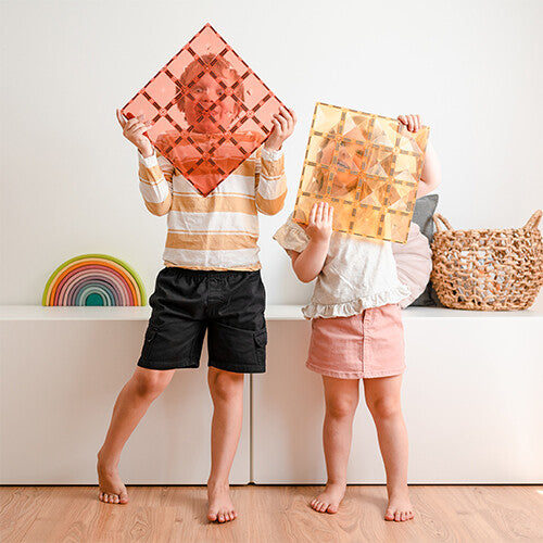 Twee kinderen kijken door Connetix pastel magnetische bouwplaten in de kleuren lemon en peach.