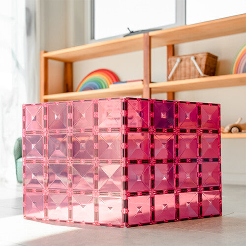 Een grote kubus gemaakt van Connetix roze en bessenkleurige magnetische bouwplaten staat op de vloer.