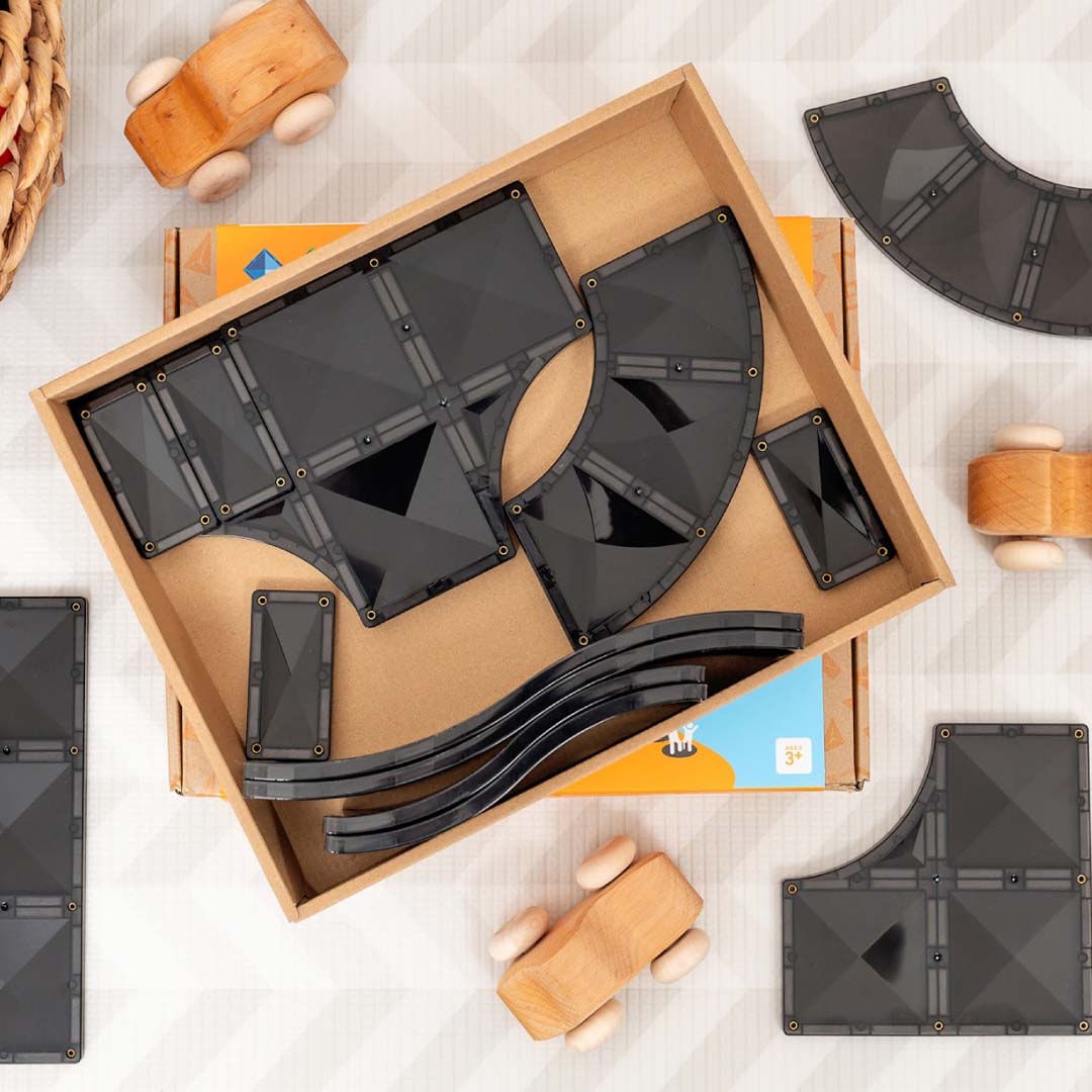 Een open doos met zwarte Connetix magnetische tegels voor wegen en drie houten speelgoedauto's.