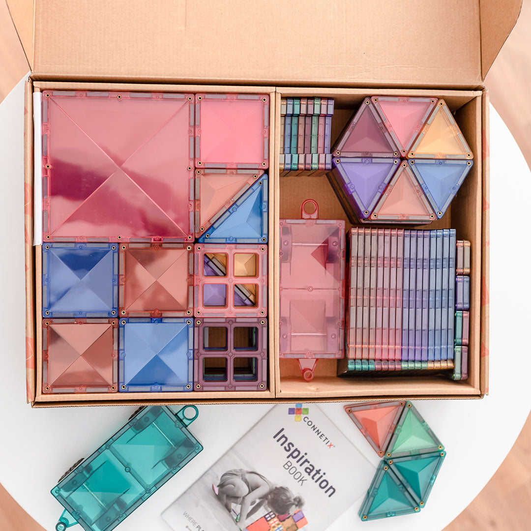 Open doos Connetix magnetische tegels in pastelkleuren, met een inspiratieboek en losse tegels ernaast.