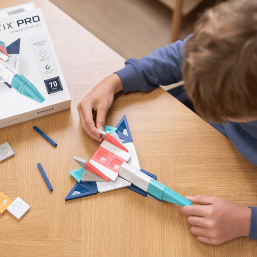 Een kind bouwt een ruimtevaartuig met Connetix magnetische tegels op een houten tafel.