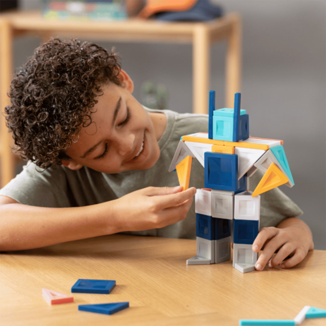 Een kind bouwt een robotfiguur met Connetix magnetische tegels op een houten tafel.