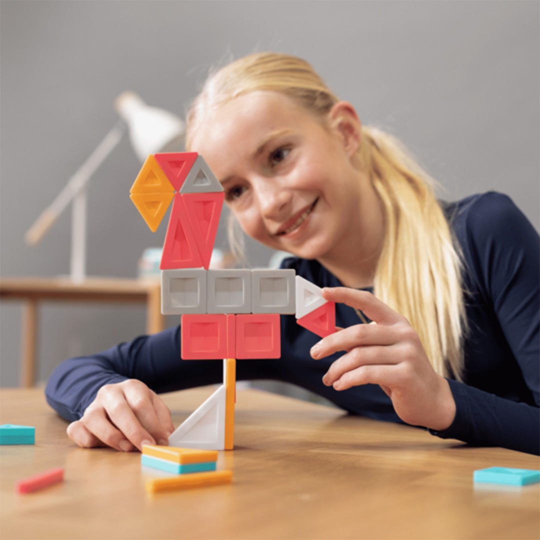 Een meisje bouwt een kleurrijke abstracte figuur met Connetix magnetische tegels.