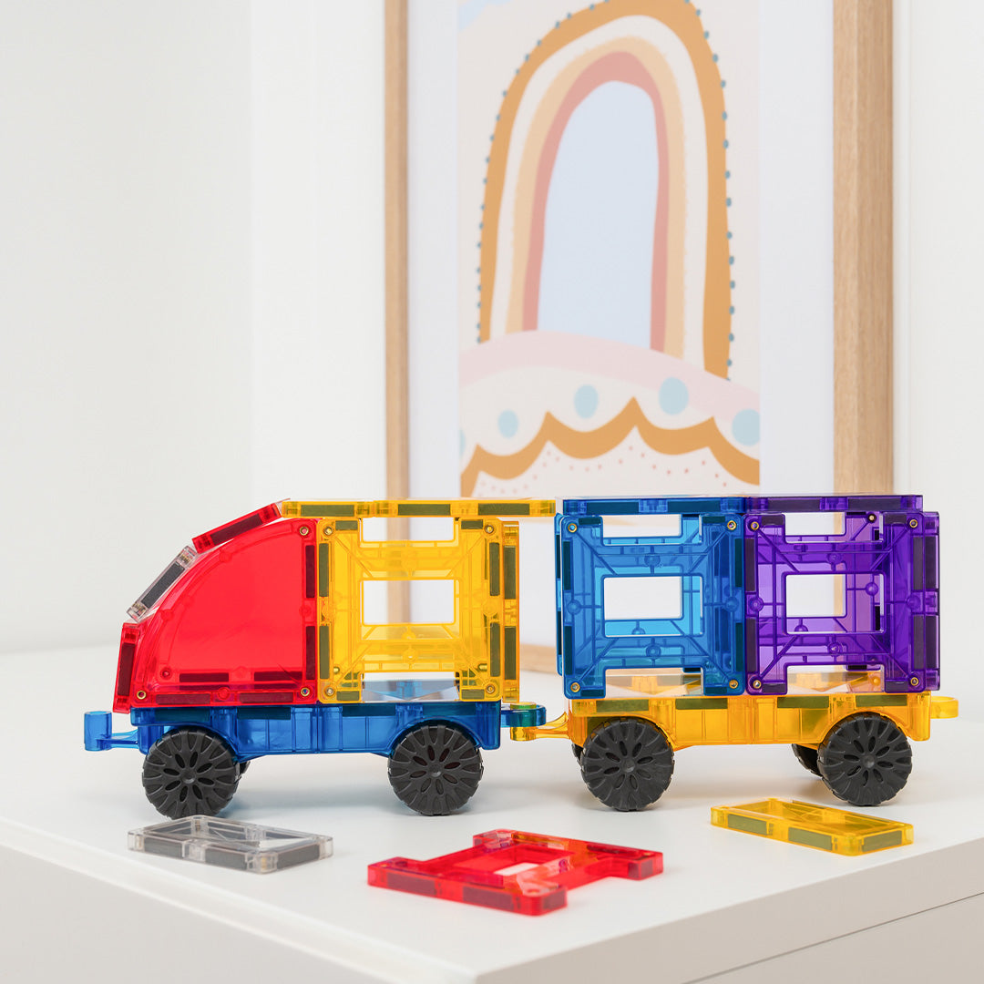 Een Connetix vrachtwagen met aanhanger, opgebouwd uit kleurrijke magnetische tegels, staat op een witte tafel.