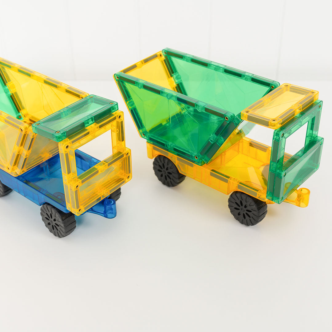 Twee Connetix vrachtwagens, gemaakt van blauwe, gele en groene magnetische tegels, staan op een witte ondergrond.