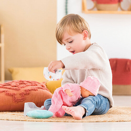 Een jongen speelt met een babypop en Corolle poppenaccessoires, waaronder een potje en doekjes.