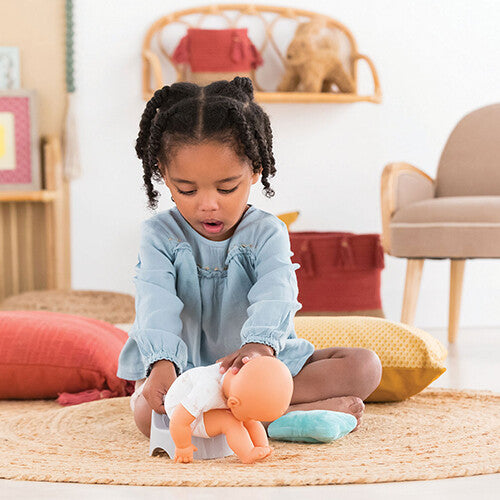 Een meisje speelt met een babypop die op een Corolle poppenpotje zit.
