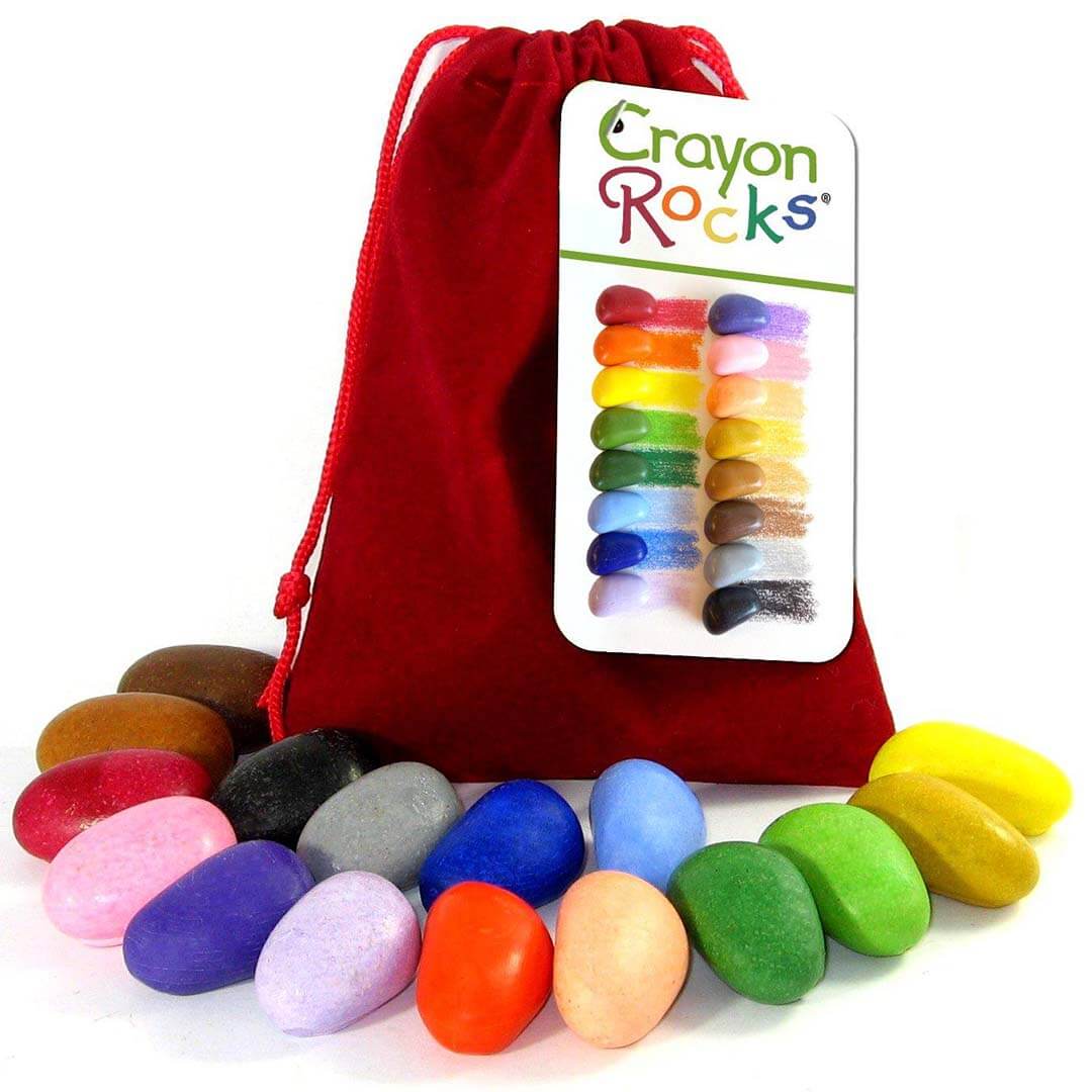 Een rode fluwelen zak met Crayon Rocks waskrijtjes en een label met kleurstalen, omringd door losse waskrijtjes.