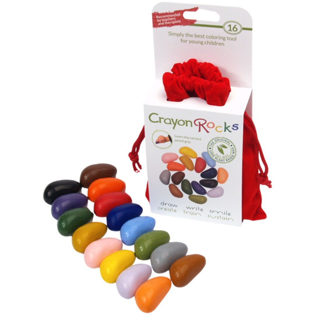 Een witte verpakking van Crayon Rocks waskrijtjes met een rode fluwelen zak en een scrunchie, met waskrijtjes ervoor.