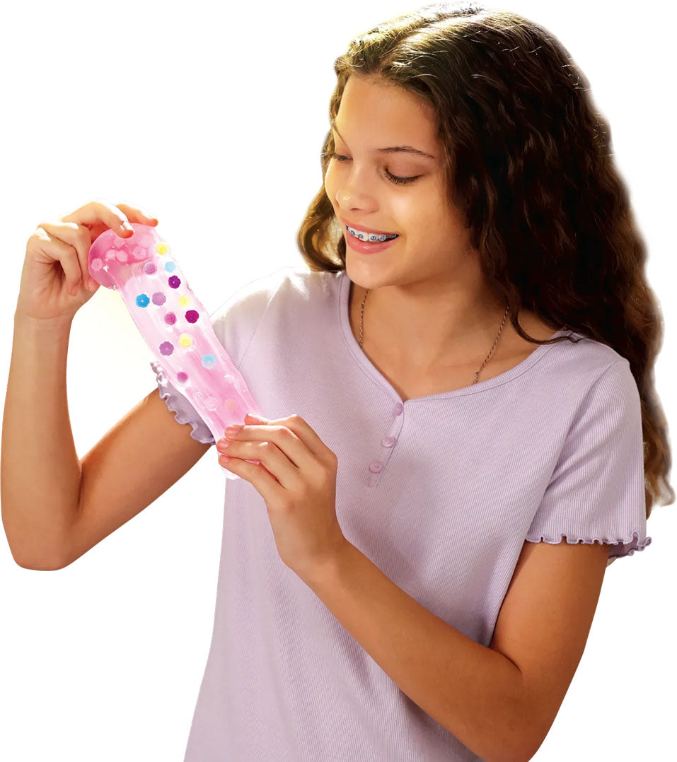Een meisje met beugel rekt roze slijm- en kleispeelgoed met gekleurde bloemvormpjes uit.
