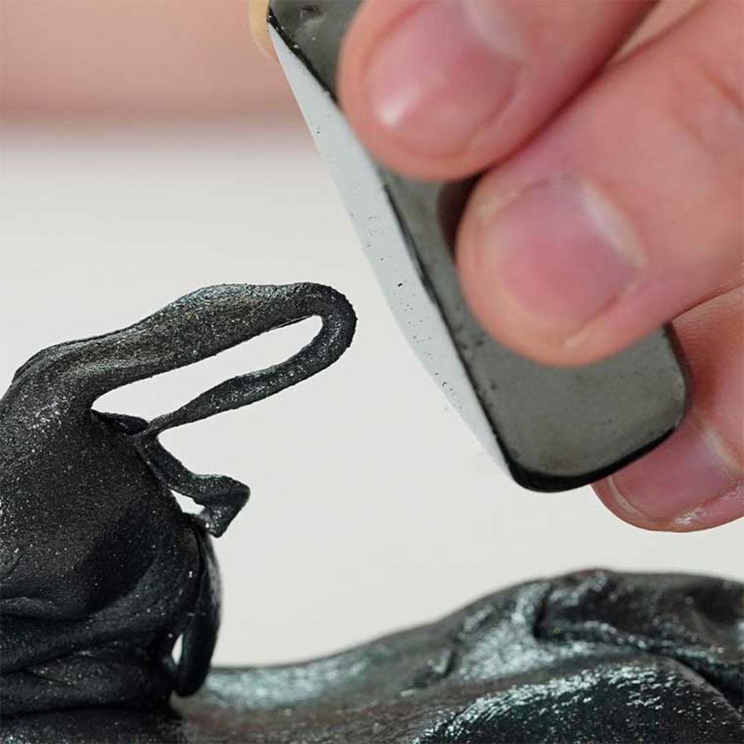 Een hand houdt een zwarte magneet boven donkergrijze magnetische klei van Crazy Aaron's, die zich uitstrekt naar de magneet.