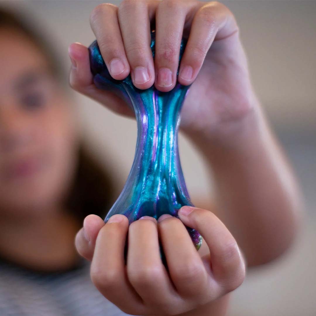 Kinderhanden rekken de iriserende blauw-paarse Thinking Putty uit.