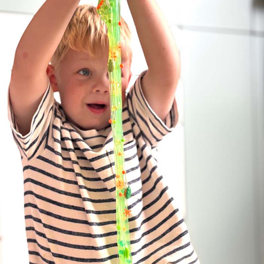 Een jongen speelt met groen Crazy Aaron's Dino Dew slijm met dinosaurusbedeltjes.