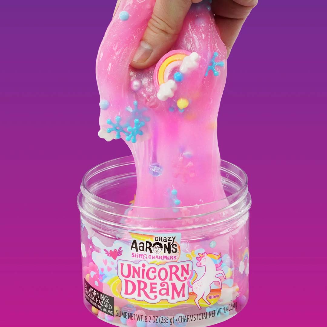 Een hand trekt roze Crazy Aaron's Unicorn Dream slijm met eenhoorn- en sneeuwvlokbedeltjes uit de pot.