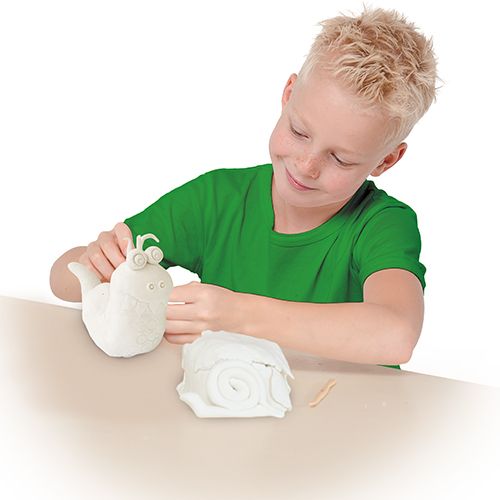 Een lachende jongen decoreert een witte slak van boetseerklei, met een stuk klei ernaast.