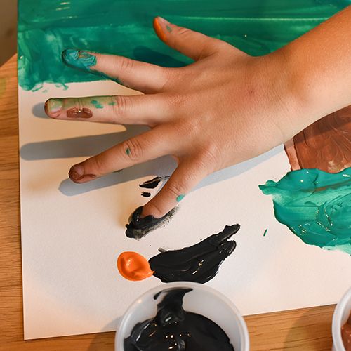 Detail van een kinderhand met Creall vingerverf op de vingers, schilderend op papier.