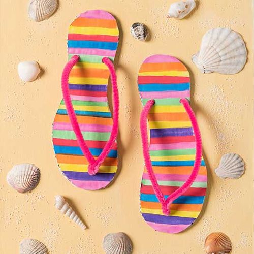 Een demonstratie van twee geknutselde, gestreepte teenslippers met roze bandjes op een zandkleurige ondergrond met schelpen.