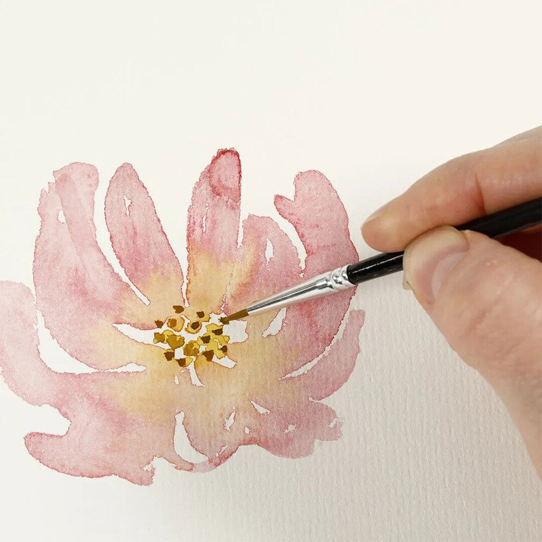 Een hand schildert met een creativ company aquarelpenseel de kern van een roze bloem op wit papier.