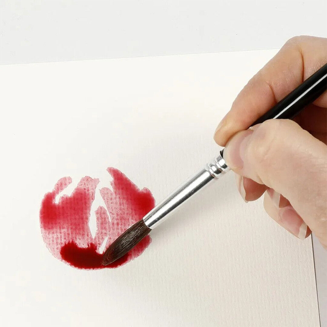 Een hand schildert met een creativ company aquarelpenseel een rode vlek op wit papier.