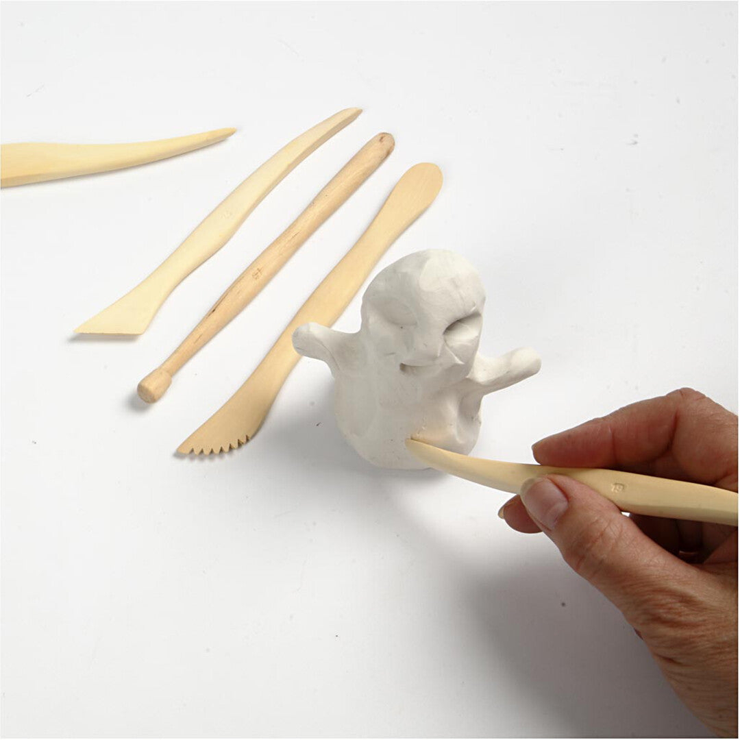 Een hand gebruikt een houten boetseergereedschap om een figuur van witte klei te vormen.