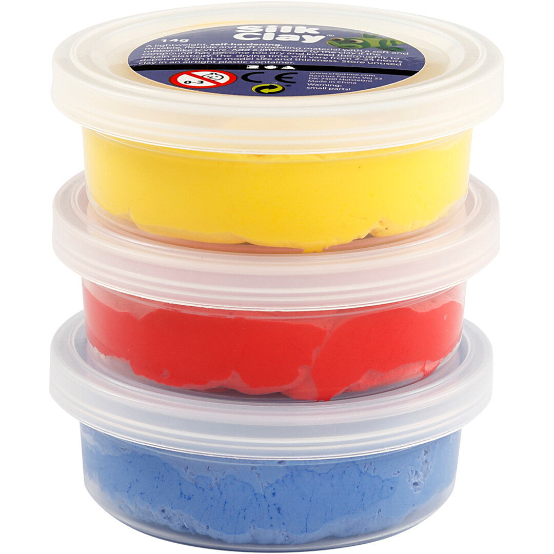 Drie gestapelde potjes creativ company Silk Clay boetseerklei in geel, rood en blauw.