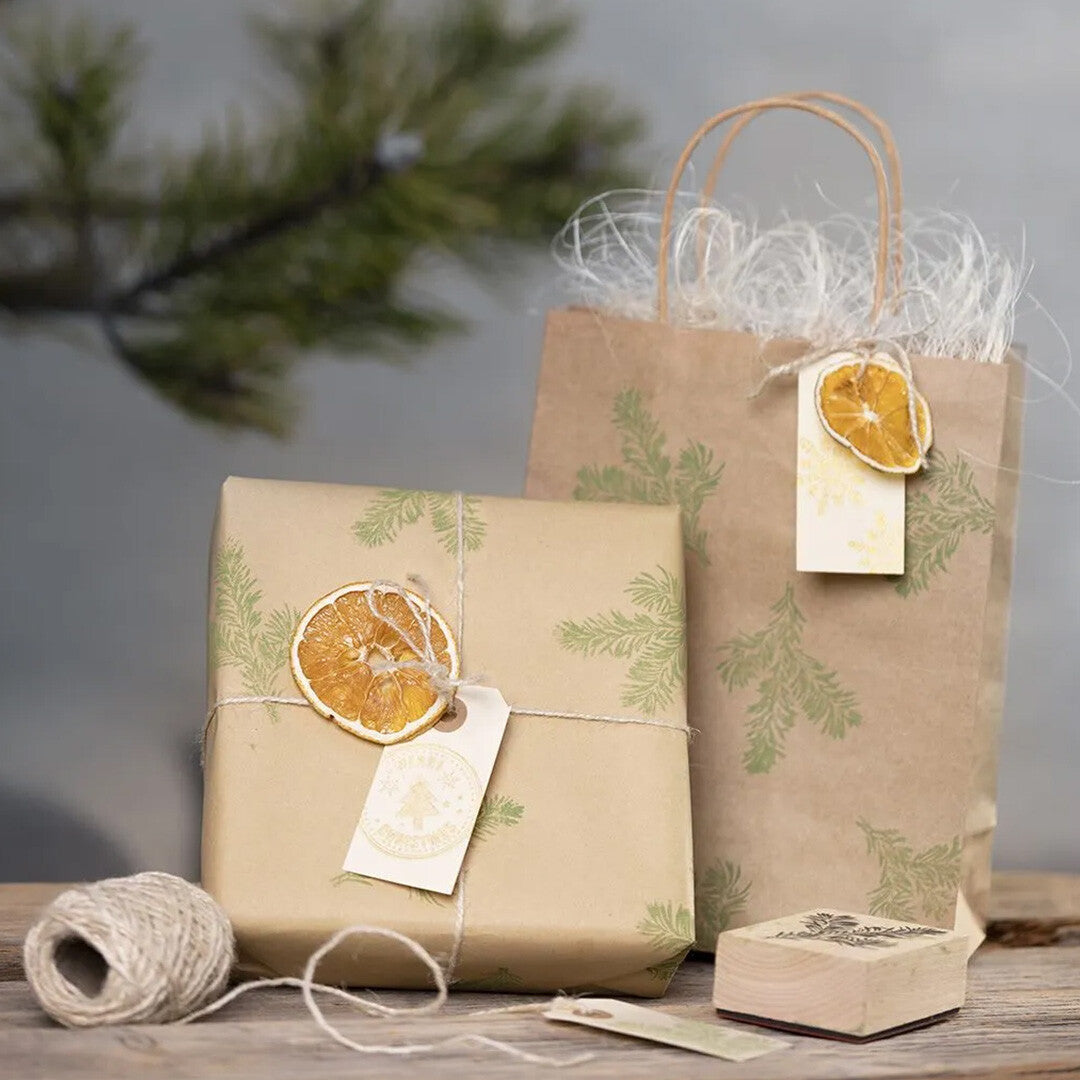 Twee ingepakte cadeaus met creativ company cadeaulabels, gedecoreerd met gedroogde sinaasappelschijfjes en dennentakken.