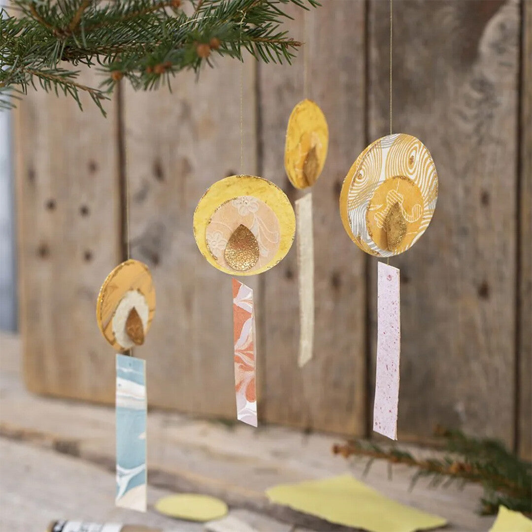 Vier hangende decoraties gemaakt van creativ company decoratie papiervormen, met ronde en rechthoekige vormen in geel en pastelkleuren.