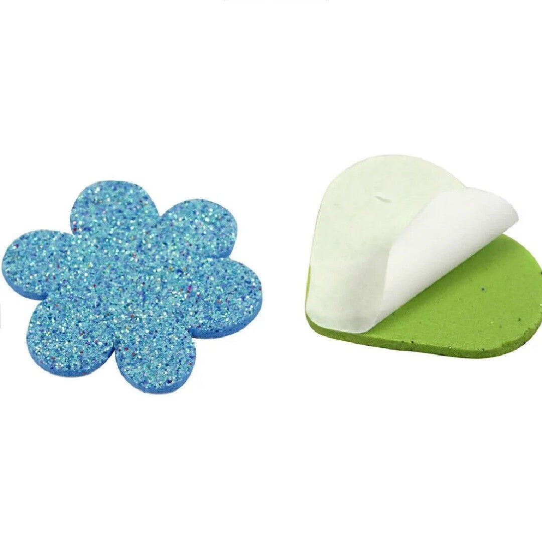 Detail van een blauwe creativ company eva foam bloemsticker met glitter en een groene hartsticker waarvan de beschermfolie van de plaklaag is verwijderd.
