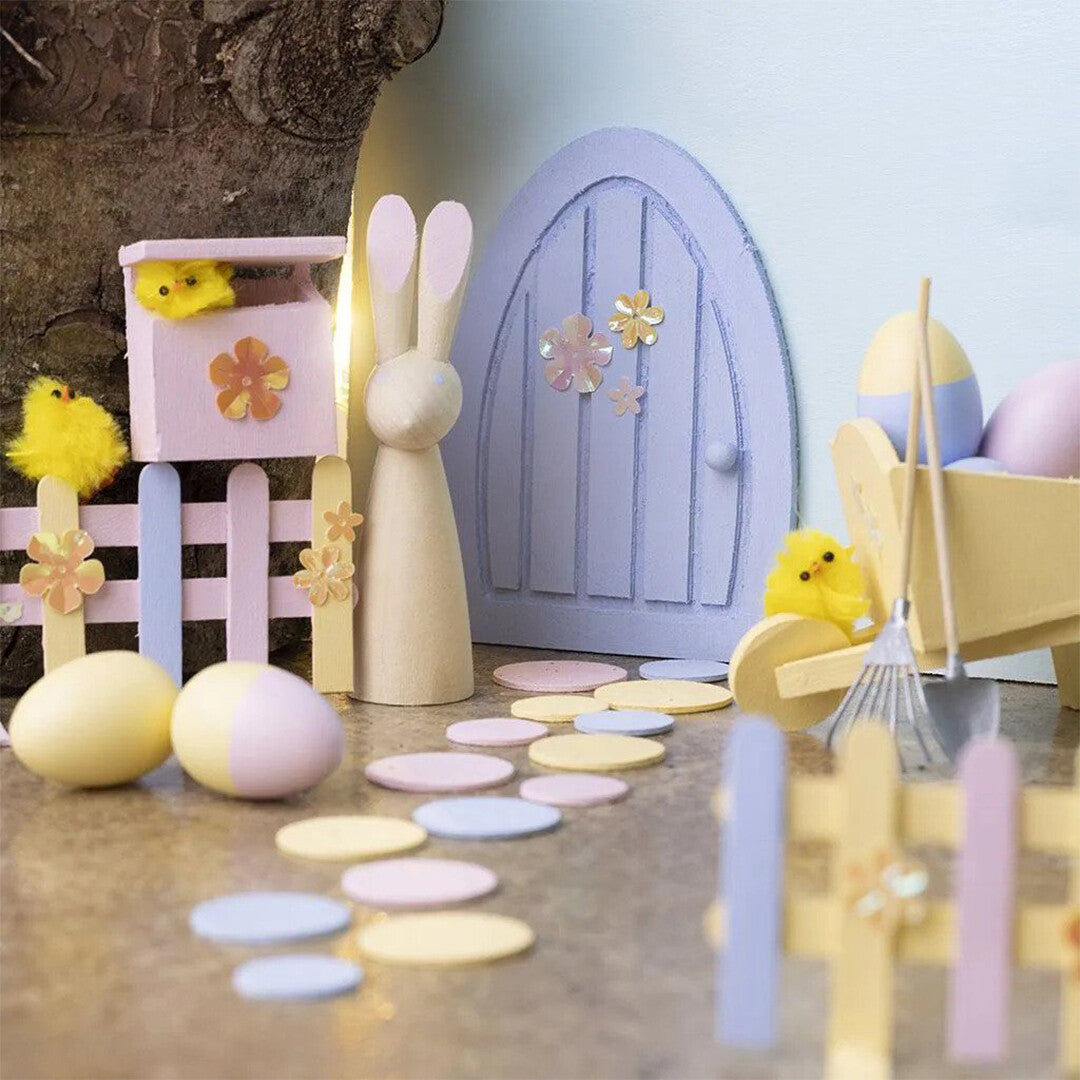 Een miniatuur sprookjestuin met houten figuren, eieren en hekjes gemaakt van ijsstokjes.