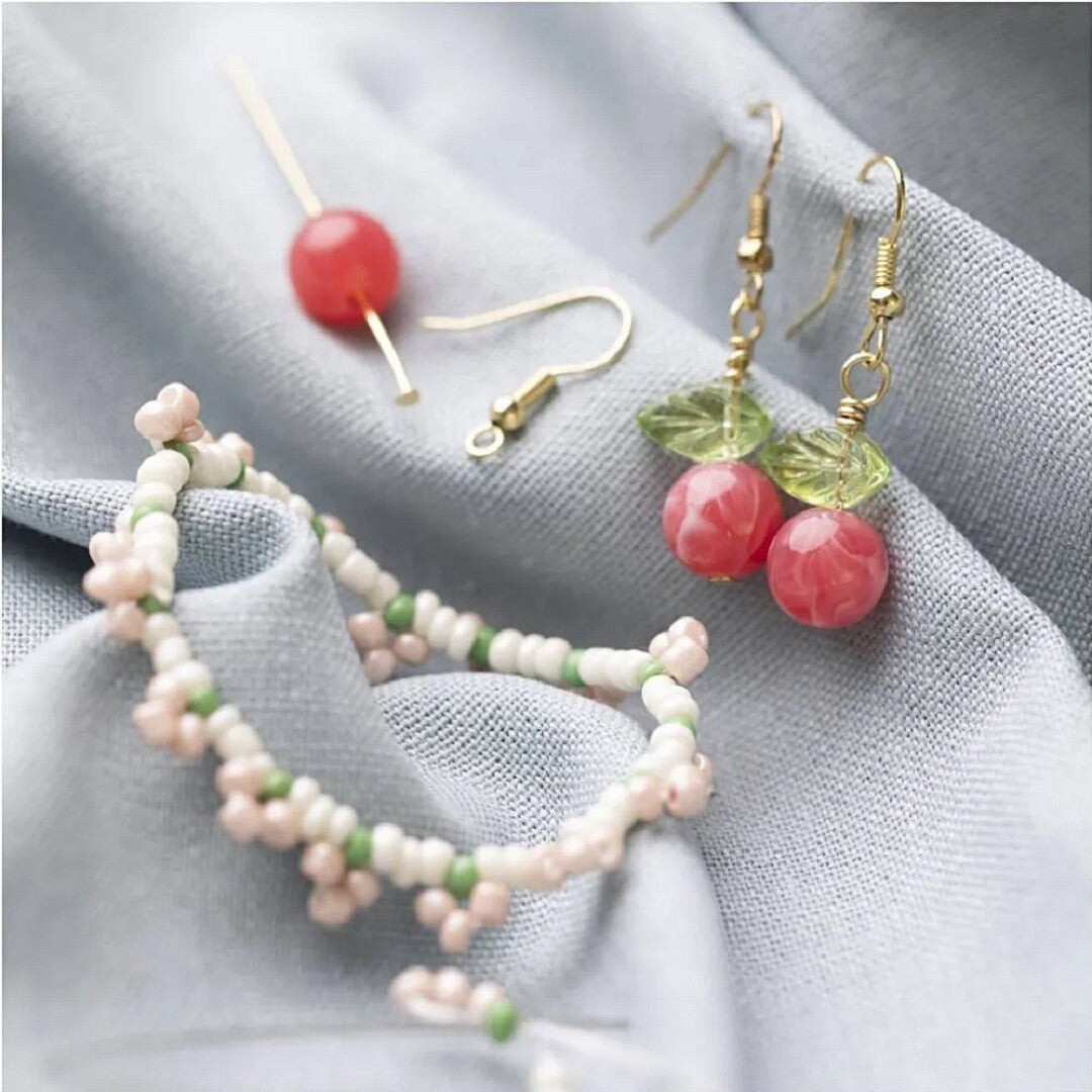 Detailfoto van een roze kralenarmband en kersvormige oorbellen, gemaakt met de sieraden knutselset.