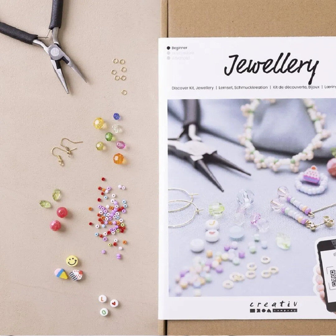 De creativ company sieraden knutselset met diverse kleurrijke kralen, metalen onderdelen, een tang en de handleiding.