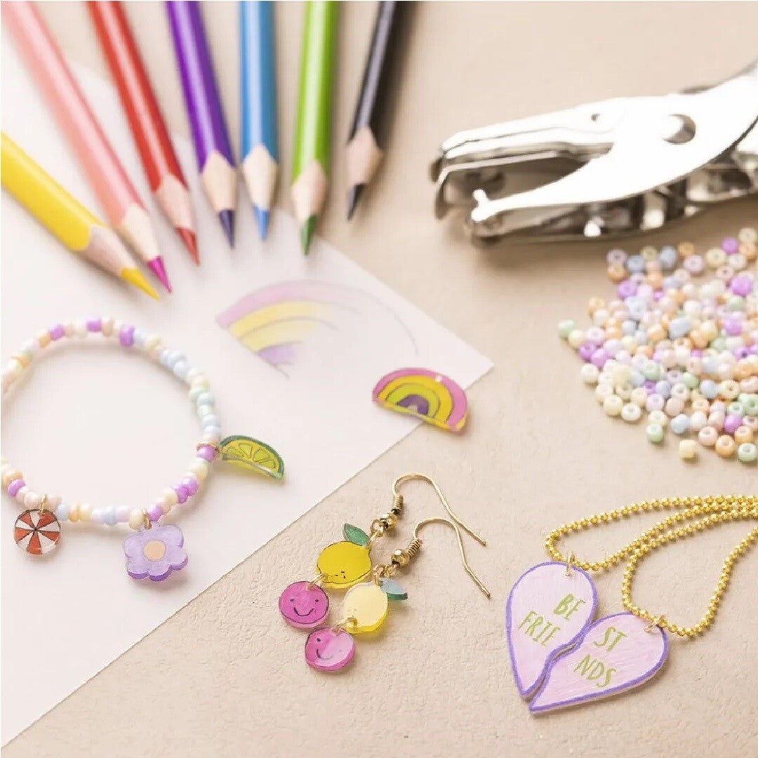 Sieraden gemaakt van Creativ Company krimpfolie, waaronder een armband, oorbellen en een ketting, met kleurpotloden en een perforator.