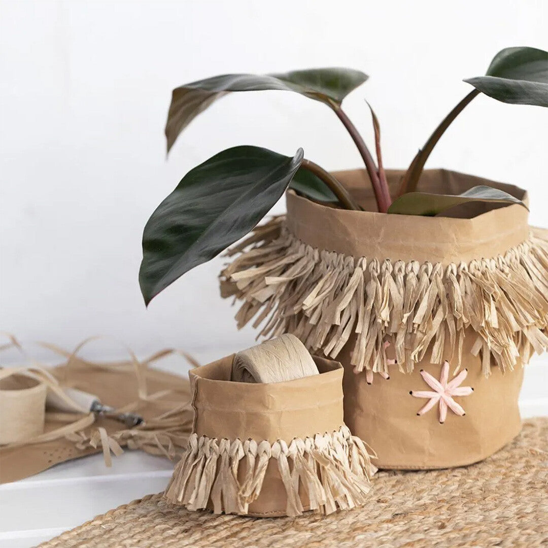 Twee decoratieve plantenpotten van papier met franjes van zandkleurig raffia papiergaren, waarvan één met een plant.