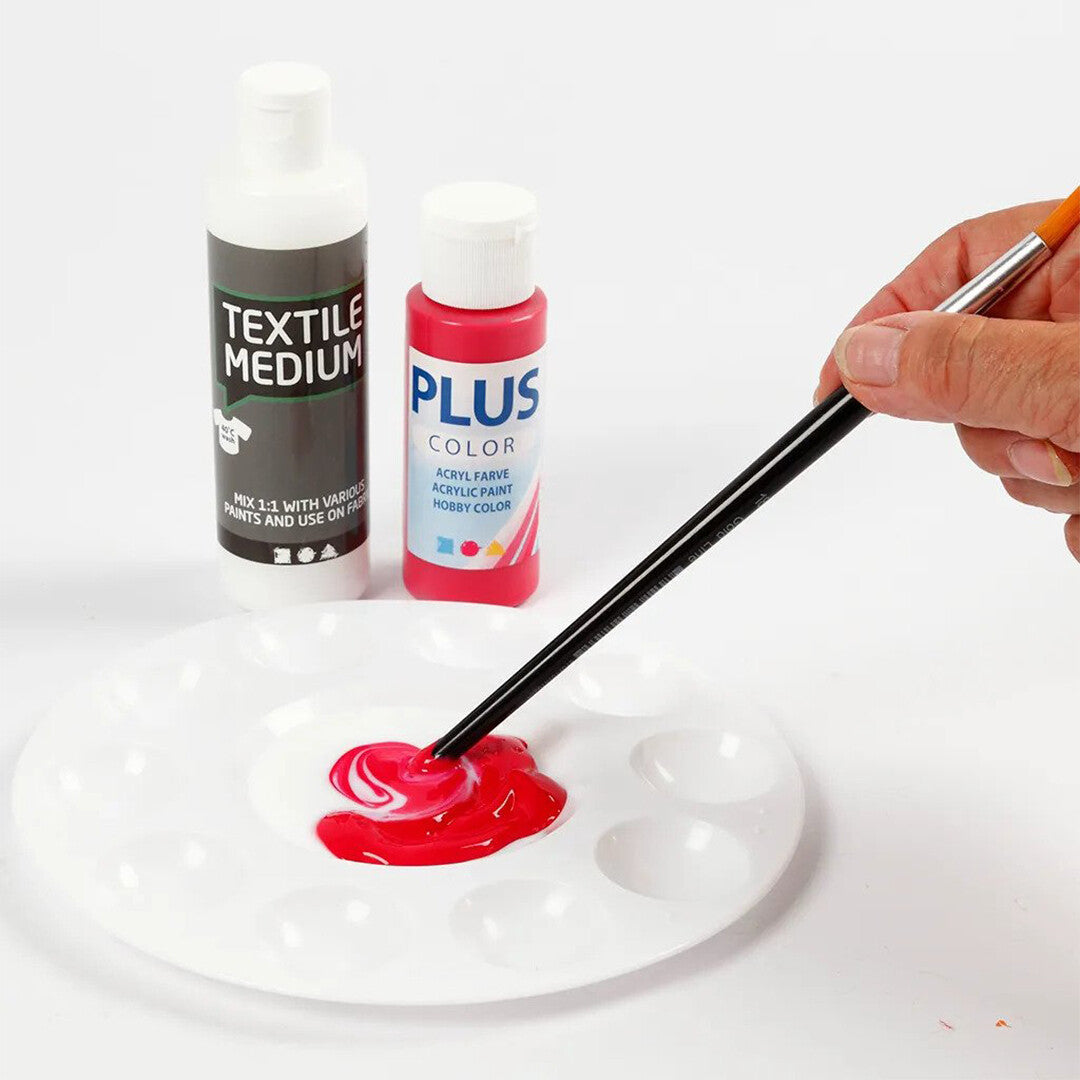 Een hand mengt rode verf op een rond wit Creativ Company schilderspalet, met verfflessen op de achtergrond.