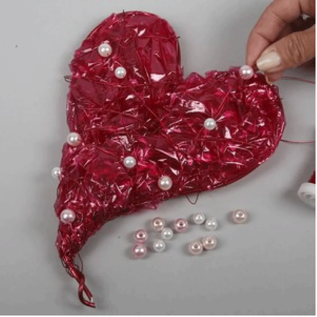 Een hand decoreert een rood hartvormig knutselwerk met parels.